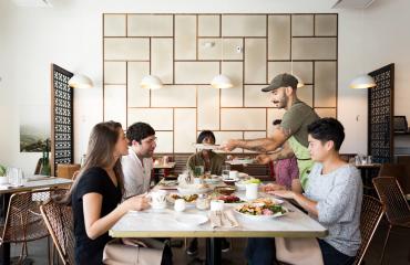 Man Serving Food To 3 People At A Table In Laziz Kitchen