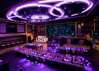A large meeting room with a long table, many chairs, a stage, and screens