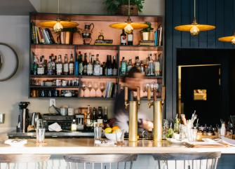 A bar with shelves of bottles and glasses, with a person behind the counter.