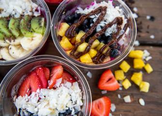 Three glass bowls of fruit and granola topped with coconut flakes and chocolate sauce