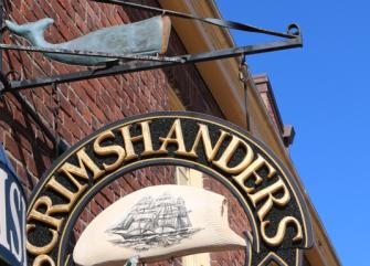A close-up of a sign with a ship image and the word 'Curimshanders' on a brick building