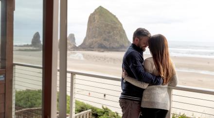 A couple stands on the balcony at the Hallmark Resort & Spa, overlooking the beach and Haystack Rock