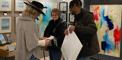 three people and one is selling a painting that is on the wall