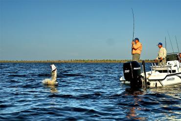 Three people on a small boat with one reeling in a tarpon in a tournament on  Charlotte Harbor