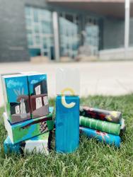 Stacked kubb featuring artist painting of Pablo Center and Eau Claire yellow "e" logo set on ground outside with Pablo Center in background