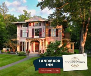 an image of a pink victorian house with a green lawn and large trees in front. the text says Landmark Inn.