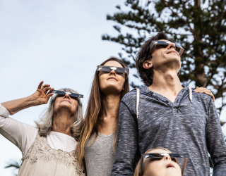 Mother, father, grandmother and granddaughter viewing a solar eclipse in the outdoors