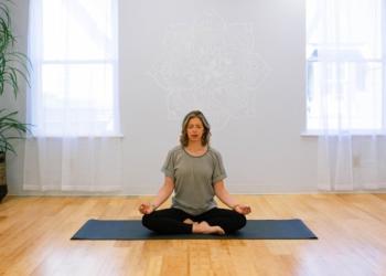 Woman sitting criss cross on a yoga mat in the center of a studio alone