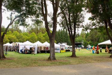Large outdoor grassy area with vendor tents surrounded by trees.