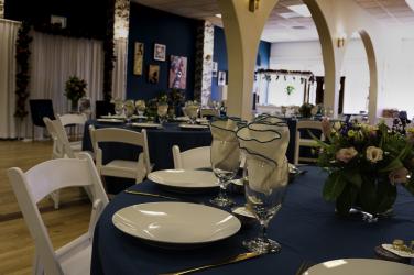Fancy table settings for an event, blue tablecloth, white dinner plates, and napkins in water glasses