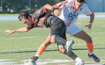Two male soccer players fighting for a soccer ball on a soccer field.