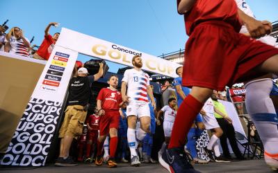 Male soccer players walking onto a soccer field from the stands.