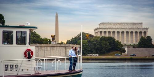 A couple on a water taxi passing the Washington Monument and Lincoln Memorial