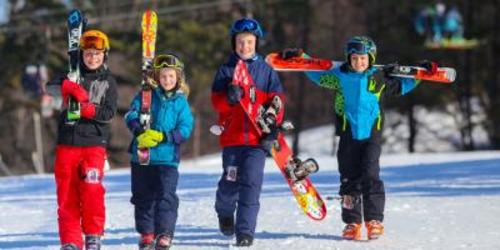 Four young kids in snow gear all carrying a set of skies or a snowboard
