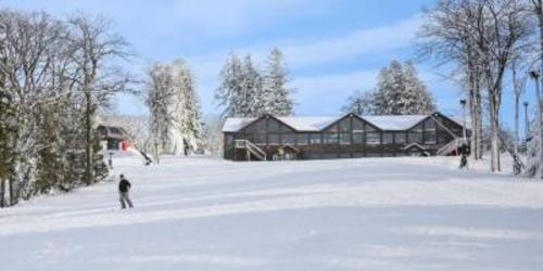 Two people skiing in front of a large brown mansion with windows at Laurel Mountain Ski Resort on a snowy day.