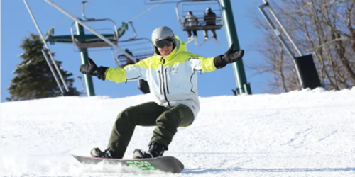Person in a yellow and white winter goat snowboarding down a hill with people on a ski lift in the background