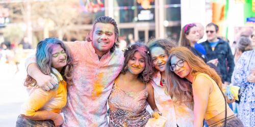Group of friends covered in colourful powders posing for a photo at Holi event 2025