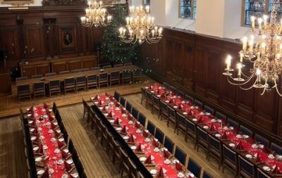 Great Hall at Clare College Cambridge set up for a festive banquet. 3 long tables with white table linen and a scarlet runner down the middle of each table. Candelbra are placed at regular intervals on each table
