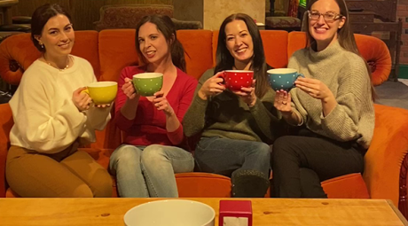 Four females pose while sitting on the orange couch at The Friends Experience in the King of Prussia Mall