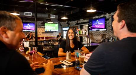 Female bartender at King of Prussia Grill & Tavern talks to two customers sitting at the bar