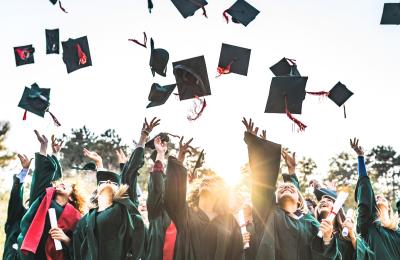 People wearing graduation gowns throwing their caps in the air - Credit Visit West