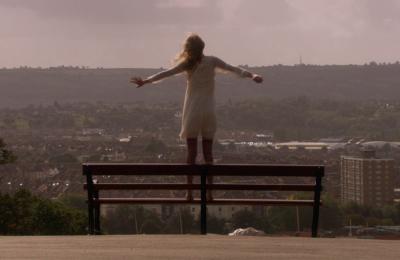 A woman standing on a bench with her arms outstretched.