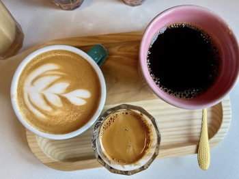 Overview of a coffee tasting flight , with a latte, a shot of espresso, and a cup of filtered black coffee on a wooden platter.