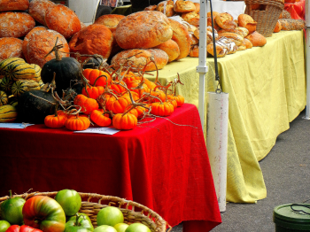 Table at a farmer's market covered in red and yellow table clothes with baked bread and pumpkins on top