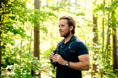 a person holds binoculars in the woods