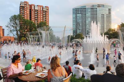People sitting at restaurant table looking over dozens of children playing in Scioto Mile fountains