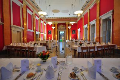 Downing College Cambridge dining hall: scarlet walls with a white ceiling. The hall is set up for formal dining with crisp white linen, candelabra, cutlery & fresh flowers