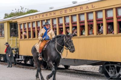 cowboy riding a horse next to a northern central railway train