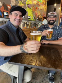 Two men smiling and drinking beer at Pour Me
