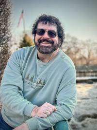 a person in sunglasses smiles and leans casually for a photo