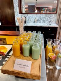 A selection of orange & green smoothies in small individual sized glass bottles set out on a wooden plinth.