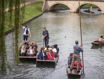 Punts on the River Cam with people in them near a stone bridge