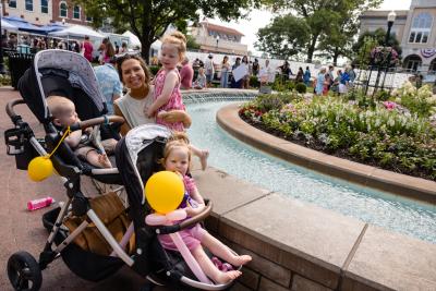 A family with a stroller and balloons in front of the fountain on the Bentonville square.
