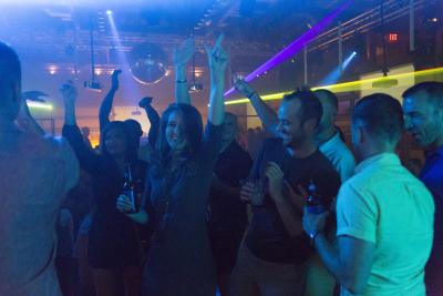Nightclub with people dancing & drinking under laser lights & disco balls