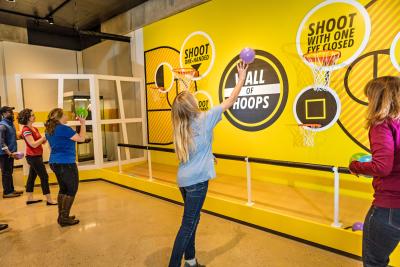 Adults and children shooting basketball hoops inside the "Ohio - Champion of Sports" exhibit at Ohio History Center