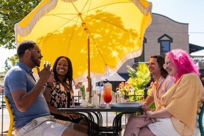 A group of people sitting at an outdoor patio table, under a large yellow umbrella