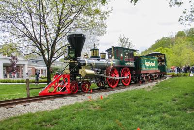 A view of the Carillon Park Railroad, showing a steam locomotive pulling a passenger car with park visitors.