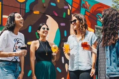 Group of four women laughing and holding colorful drinks in front of a vibrant mural, enjoying a sunny day in Cumberland County, NC together.