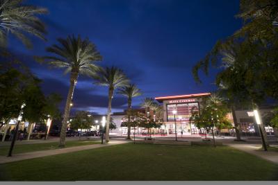 Photo shows exterior of Maya Cinemas Movie Theater with row of palm trees and grass area.