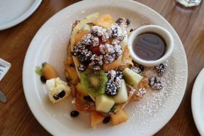 Plate of French toast with sliced fruits and powdered sugar on top
