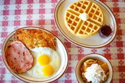 Plate of waffles and a plate of eggs, ham and hash browns on table