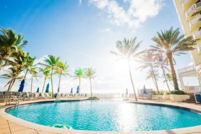 The beachfront pool at the Pelican Grand Hotel, looking east to the sun over the Atlantic Ocean with palm trees on both sides of the pool