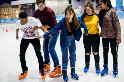 Group of friends trying to ice skate and helping each other from falling over