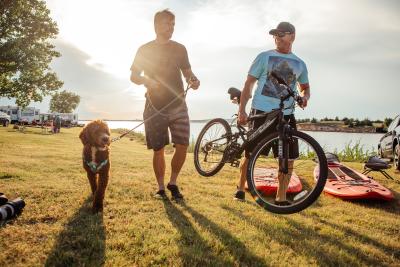 A labradoodle on a leash next to its owner and a man with a mountain bike