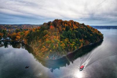 Aerial photo of Snake Hill on Saratoga Lake in autumn with foliage and a boat skimming along the water.