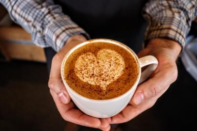 hand holding mug of coffee with heart design and sprinkled cinnamon